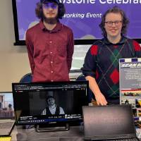 Two students posing for photo behind booth